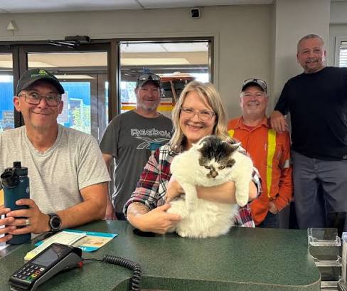 Five Mercer Fuels staff members at the office counter, with a cat held in the centre.