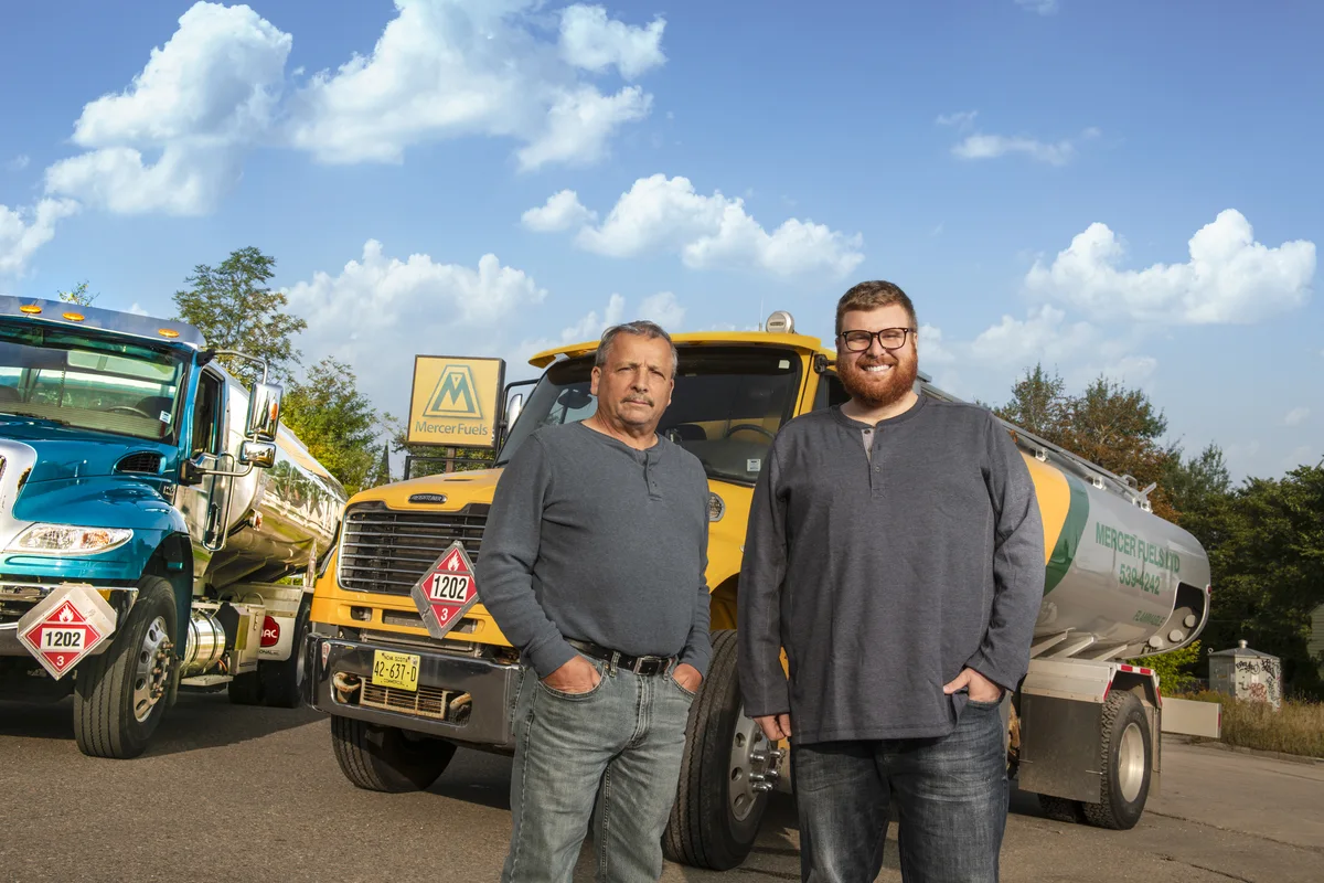 Two men standing with Mercer Fuels delivery trucks.