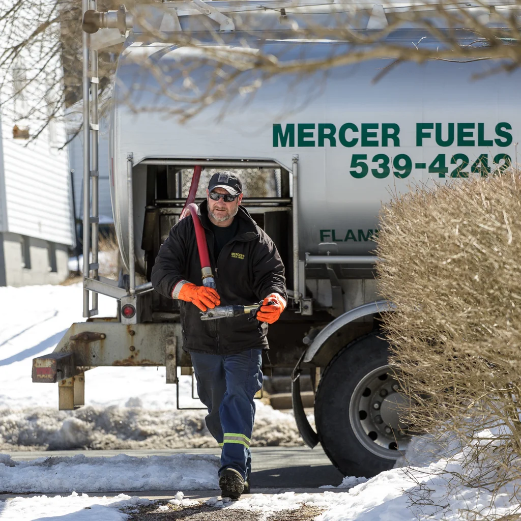 Mercer Fuels driver carrying a delivery hose beside a fuel truck.