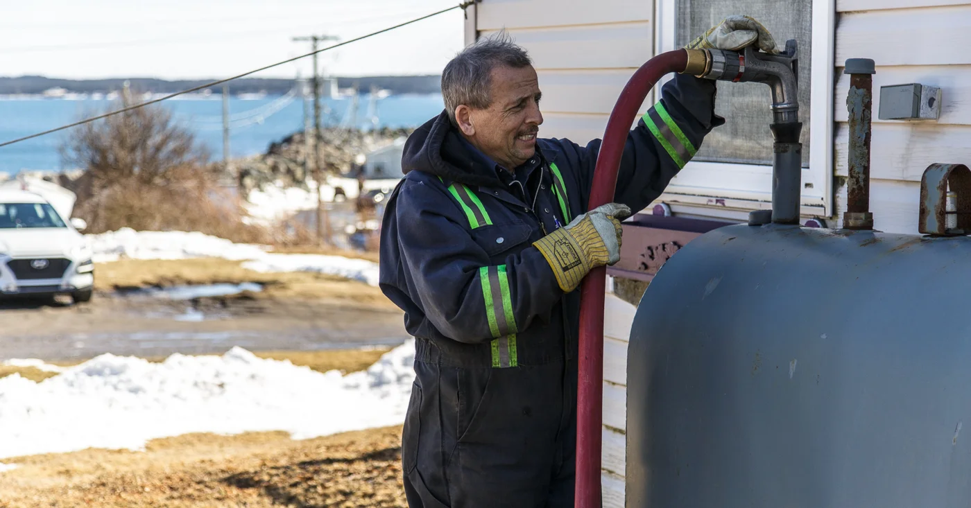 Driver connecting a delivery hose to an outdoor oil tank beside a home.