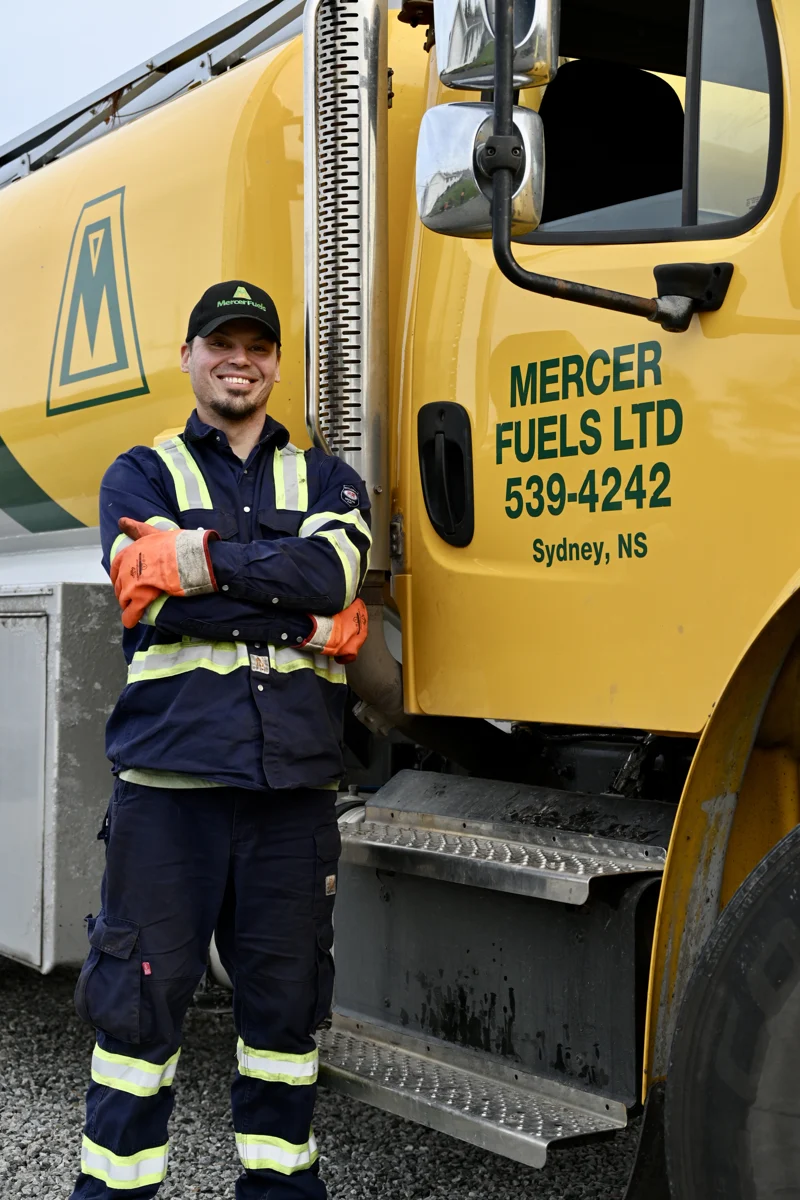 A Mercer Fuels worker standing beside a yellow delivery truck.
