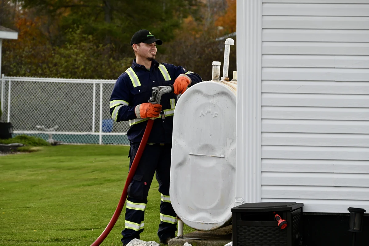 A Mercer Fuels delivery worker filling an outdoor heating oil tank beside a home.